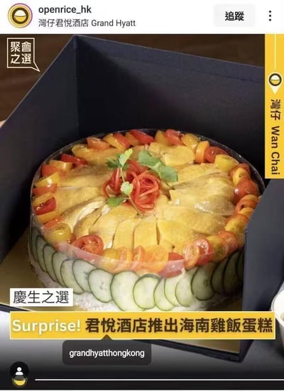 这是一张来自美食社交平台的截图，展示了香港湾仔君悦酒店推出的创意菜品——海南鸡饭蛋糕。这款“蛋糕”打破了大众对蛋糕甜口的固有认知，将经典海南鸡饭以蛋糕的形式呈现：上层是切分整齐的海南鸡肉，搭配彩椒、小番茄作为装饰，下层边缘环绕着切片黄瓜，底部是米饭，整体被放置在蛋糕盒中，既保留了海南鸡饭的风味，又适配了庆生、聚会的场景需求，是极具创意的咸口“蛋糕”。图中没有双关或谐音梗，核心亮点在于将传统餐食进行形式创新，满足不同场景的用餐需求。