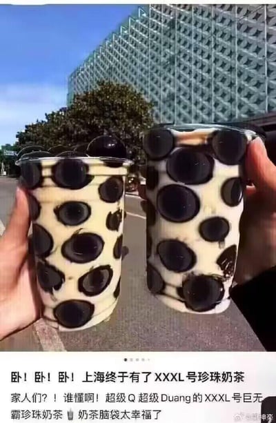 这是一张创意修图作品，画面中两只手分别举着两杯奶茶，奶茶杯里的珍珠被处理成夸张的超大尺寸，部分珍珠甚至从杯口凸起，视觉效果极具冲击力。图片下方配有激动的文案，声称上海推出了XXXL号巨无霸珍珠奶茶，形容珍珠超级Q弹有嚼劲，表达了奶茶爱好者的兴奋心情。实际上这是一张通过后期修图制作的搞笑图，并非真实存在的饮品，利用夸张的视觉效果来调侃奶茶爱好者对珍珠奶茶的喜爱。