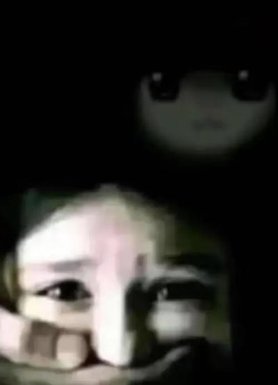 图片中显示一个人用手捂住部分面部，眼睛睁大看向镜头。画面上方有一个模糊的白色圆形物体，带有两个黑色圆点，类似眼睛的图案。整体图像光线昏暗，画质较模糊，营造出一种神秘的氛围。