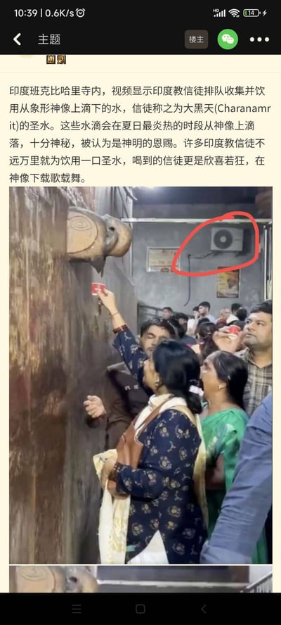图片显示一群印度教信徒在庙宇内排队，使用小杯子接取大象形神像流下的“圣水”。画面右上方被红圈标记了一台风扇，与信仰场景形成强烈反差。墙上有一些标语或说明，画面氛围庄重但又因突出风扇的存在有些幽默感。

该图片有明显“现实与信仰冲突”的双关意味，通过突出风扇的现代设施，映射宗教仪式与现实环境的碰撞。
