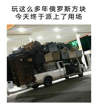 这是一张在加油站拍摄的实拍图，画面中一辆白色皮卡被各类家具、箱子等物品堆满，物品如同俄罗斯方块一般被尽可能地填充在皮卡上，导致车头被压得翘起，车身严重倾斜，看起来摇摇欲坠。图片上方配有文字“玩这么多年俄罗斯方块今天终于派上了用场”，将这种极致利用空间的装载方式和俄罗斯方块的玩法关联起来，用夸张搞笑的方式调侃搬家时充分利用车辆空间的行为，充满了幽默的反差感。