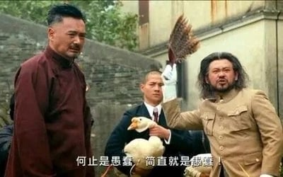 这是一张基于电影《让子弹飞》剧照进行P图改编的静态搞笑图，创作者将原场景中的枪械替换为一只大白鹅，右侧的人物做出举着鹅翅膀当作枪的夸张姿势，同时搭配字幕“何止是愚蠢，简直就是愚蠢”，通过荒诞的道具替换和重复的吐槽文字，制造出强烈的反差喜剧效果，生动地表达了对他人愚蠢行为的讽刺与调侃，画面充满戏谑感。