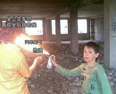 这是一张经过文字加注改编的真人搞笑梗图，画面场景设定在一个空旷的废弃建筑内部，地面满是碎石。画面右侧的男孩手持喷雾罐，与左侧的人配合，制造出火焰喷射的效果；火焰被标注为“汽车尾气 热浪”，画面上方配文“坐公交车总喜欢坐后排的我”。这张图用夸张的火焰喷射场景，生动又搞笑地调侃了喜欢乘坐公交车后排的人群，常会被车辆尾气以及后排区域的热浪“袭击”的真实通勤体验，将日常通勤中的小困扰以幽默的方式放大呈现。