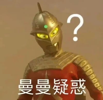 图片中是奥特曼角色，身着银色头盔（头盔顶部有尖角，中央有绿色指示灯）和红色铠甲，黄色双眼瞪大，表情疑惑。角色右侧有一个白色问号，下方配有文字“曼曼疑惑”。整体画面背景为单一的浅棕色，通过角色的困惑表情、问号符号及文字，直观表达出疑惑的情绪，常用于网络交流中表示对某事的不解。