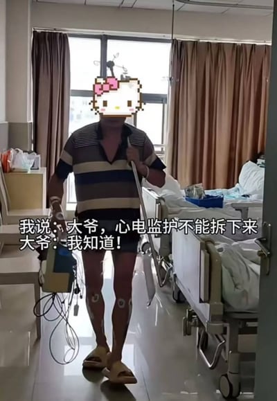 医院病房场景中，一位穿着条纹短袖和短裤的大爷，腿上还贴着电极片，一手拄着拐杖，另一手提着心电监护仪正在行走。图片配文展现了医护人员提醒大爷不能拆下心电监护，但大爷却坚持带着仪器行走的有趣对话，形成一种明知故犯的幽默效果。大爷的面部被像素化的Hello Kitty图案遮挡以保护隐私。