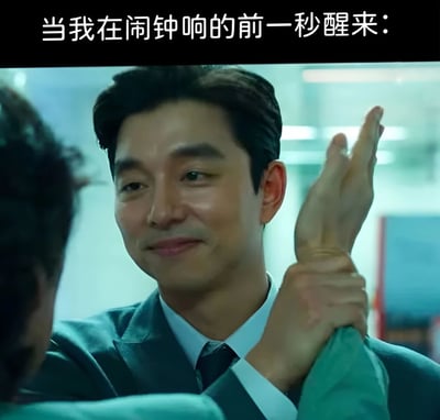 图片上方配有文字“当我在闹钟响的前一秒醒来：”，下方是韩国演员孔刘在电视剧《Goblin》中的剧照。他穿着西装，面带自信从容的微笑，正握住另一个人的手腕，姿态显得掌控力十足。这张梗图通过孔刘角色的自信形象，幽默地表达了人们在闹钟响起前一秒醒来时那种侥幸又得意的心理状态，仿佛自己掌控了时间。