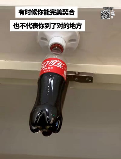 图片展示了一个倒挂的可口可乐瓶，其红色瓶盖恰好插入上方一个白色容器的出液口，形成了物理上的完美契合。瓶身呈深褐色，标签为红色的“可口可乐”经典标志，容器固定在浅色的橱柜下方。图片顶部配有两行白色背景黑色文字：“有时候你能完美契合 也不代表你到了对的地方”，通过日常物品的意外贴合场景，隐喻人生中“形式上的匹配不等于本质上的正确”这一哲理。
