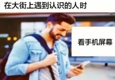 图片展示了一位穿着蓝色牛仔衬衫、背着背包的男子，他正低头微笑着看手机屏幕。图片上方配有文字“在大街上遇到认识的人时”，右侧文字标注“看手机屏幕”，幽默地描绘了人们为避免社交尴尬而假装专注于手机的常见日常行为。