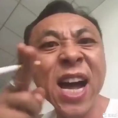 这是一张中文互联网知名梗人物神鹰哥（神鹰黑手哥）的经典特写梗图，画面为近距离大头拍摄，背景是浅色瓷砖墙面，神鹰哥情绪激动亢奋，眉头紧皱大张着嘴，正对着镜头喊话，夹着香烟的手伸出手指指向镜头方向，整体表情张力极强，是抽象区常用的梗素材。