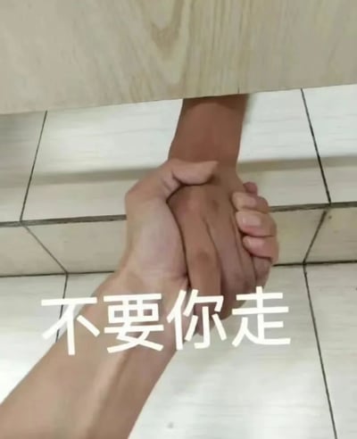 图片展示了两只手在瓷砖地面上紧紧相握的特写镜头，上方能看到木质家具的底部边缘。画面中央有醒目的白色文字“不要你走”，整体营造出一种挽留、不舍的情感氛围。这张图片通过手部动作和文字结合，直观地表达了希望对方留下的强烈情感。