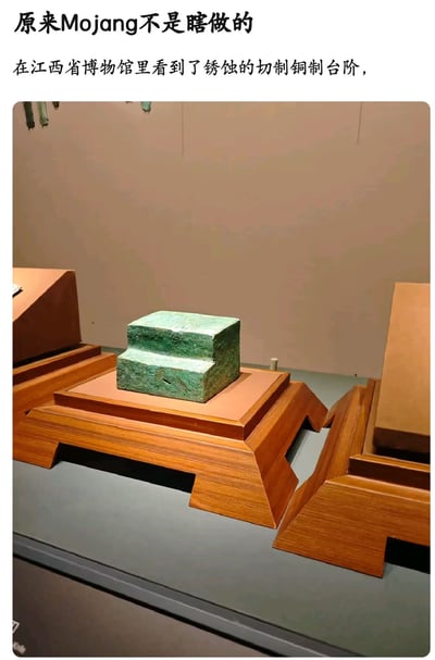 这是一张图文结合的静态实拍图，顶部配有两行玩梗文案，内容为“原来Mojang不是瞎做的 在江西省博物馆里看到了锈蚀的切制铜制台阶”。图片下方主体是江西省博物馆的展品展陈场景，一件带有青绿色铜锈的两层台阶状铜制文物放置在棕色木质展台上，该文物的造型、色泽都和知名游戏《我的世界》中由Mojang设计的氧化切制铜台阶道具高度相似，文案以此调侃Mojang的游戏道具设计并非凭空创作，而是有现实参考，很容易引发游戏爱好者的共鸣。