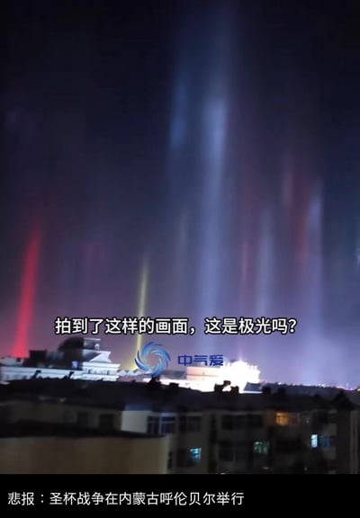 这是一张气象视频截图，画面展示了内蒙古呼伦贝尔夜空中出现的罕见寒夜光柱现象，彩色光柱垂直射向夜空，画面配文询问“拍到了这样的画面，这是极光吗？”，底部被网友添加玩梗文字“悲报：圣杯战争在内蒙古呼伦贝尔举行”，结合《Fate》系列中圣杯战争的召唤光柱设定，将罕见的大气光学现象调侃成圣杯战争的场景，制造出搞笑的反差效果。实际上该现象是寒夜光柱，是当空气中的冰晶反射地面灯光形成的大气光学现象，并非极光。