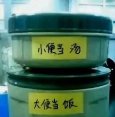 这张静态图片展示了两个上下叠放的便当盒，上方体积较小的便当盒贴有黄色标签，手写文字为“小便当汤”；下方体积较大的便当盒同样贴有黄色标签，手写文字为“大便当饭”。该内容利用文字断句的歧义制造谐音梗，原本的表述应为“小（便当）汤”“大（便当）饭”，却通过故意的文字写法引导观者产生不雅的联想，以此制造出荒诞搞笑的效果，这类趣味创作常出现在职场带饭或日常生活场景中，用来调侃和增添生活趣味。