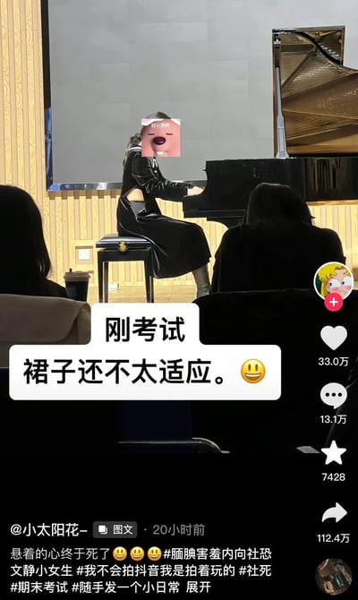 这张抖音截图表现了一位女生在钢琴考试舞台上弹钢琴，她的表情被用表情包遮挡，文字说“刚考试 裙子还不太适应。😃”。台下有人观演，场景略带紧张与幽默，透露出考场的不安和对服装的微妙吐槽。

有轻微的自嘲成分，通过自黑展现面对考试的不适与社交压力。没有明显双关或低俗梗。