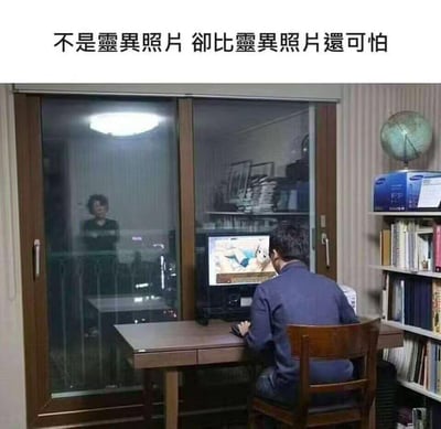 图片展示了一个令人不安的居家场景：一名男性正专注地坐在电脑前，屏幕上显示着动画内容。然而，通过他身后的玻璃门，可以看到一名女性正静静地站在那里注视着他，形成了强烈的视觉冲击和心理恐惧感。这种日常生活中被窥视的场景，比传统灵异照片更能引发观众的共鸣和不安。
