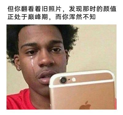 这是一张用来调侃颜值变化的网络梗图，图上方配有文字“但你翻看着旧照片，发现那时的颜值正处于巅峰期，而你浑然不知”，图中主体是一位穿着红色上衣的黑人男性，他脸上挂着清晰的泪痕，手持金色苹果手机，表情悔恨又带着不敢置信，生动地诠释了人们在翻看自己旧照片时，突然意识到自己曾经处于颜值巅峰却毫无察觉，如今颜值下降的懊悔与自嘲心情，戳中了很多人对自身颜值变化的感慨。