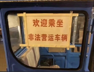 这张图拍摄了一辆蓝色车辆的车窗区域，车窗上用简易木架固定着一块手写标语牌，上面清晰写着「欢迎乘坐 非法营运车辆」。这种直白自曝车辆非法营运属性的标语形成了强烈的反差感，打破了人们对非法营运者刻意隐瞒的固有印象，显得十分搞笑。