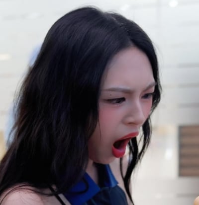 图片中展示了一位拥有浓密黑色长发的女生站在现代感十足的室内环境中。她身穿蓝色领子的服饰，背景有模糊的光线和可能是墙饰，氛围偏向机场、商场等公共场所。画面整体风格生活化，没有明显的搞笑、双关或暗示内容。适合作为日常生活类图片使用。