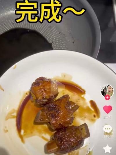 这张图是短视频平台的内容截图，画面上方配黄色描黑边的文字“完成~”，展示博主做完菜的成果：白色盘子里放着三块挂着浓郁红烧酱汁的带骨块状食物，盘子后方露出一口使用后残留污渍的不粘锅；画面右侧保留了短视频平台的交互组件，依次是博主头像关注按钮、2.4万点赞、2204条评论、收藏按钮。这三块烹制好的食物外形特殊，很容易让观看者产生不雅的联想，和发布者“完成”的得意感形成搞笑反差。
