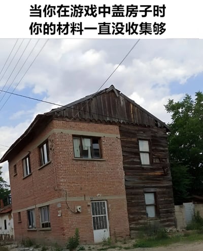 图片上方配有文字“当你在游戏中盖房子时 你的材料一直没收集够”，下方是一张现实中的未完工房屋照片。房屋左侧为红砖结构，右侧为木质结构，屋顶部分瓦片缺失，整体呈现出明显的“烂尾”状态，背景是多云的天空和几棵绿树。通过现实中未完工的建筑形象，幽默地比喻了游戏中因材料不足导致建筑无法完成的无奈场景。