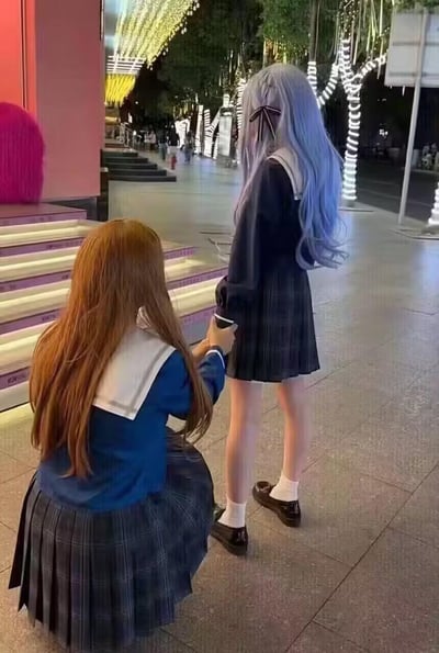 夜晚的城市街头，一位棕发JK少女蹲在地面，握着另一位蓝发JK少女的手腕，两人都身着水手领款式的JK制服，背景是装点着灯带的街道，整体氛围温馨治愈，尽显闺蜜间的亲密互动。