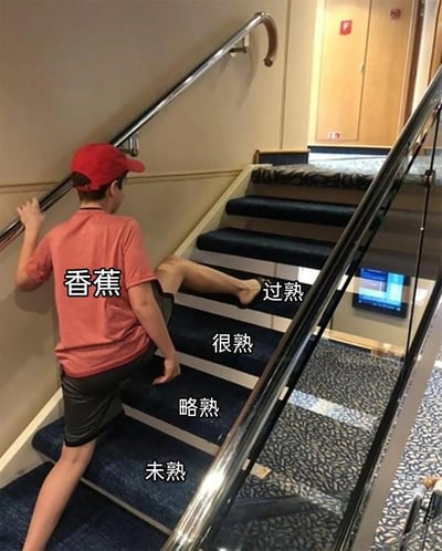 图片中一名戴着红色帽子、穿着红色T恤和深色短裤的男孩正在爬楼梯。楼梯的台阶从下到上依次标注着“未熟”“略熟”“很熟”“过熟”的文字，男孩身旁则标注着“香蕉”二字。整体画面通过将爬楼梯的动作与香蕉成熟度等级进行趣味类比，营造出轻松搞笑的效果，属于典型的生活场景创意改编梗图。