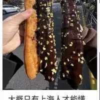图中两只手分别拿着两根长条形面包，一根是浅棕色面包体裹着巧克力涂层并撒有坚果碎，另一根是深棕色巧克力涂层搭配坚果碎。图片底部配文「大概只有上海人才能懂」，这种长条形巧克力面包是上海的特色怀旧美食，承载着不少上海人的童年回忆，只有本地人才对其有特殊的情怀与熟悉感，以此唤起上海本地人的共鸣。