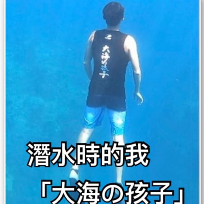图片中展示了一位正在水下潜水的男子背影。他穿着黑色背心，上面有白色的日文文字，搭配蓝色泳裤。图片下方有白色文字："潜水時的我「大海の孩子」"，表达了潜水者自称为"大海的孩子"的幽默意境。