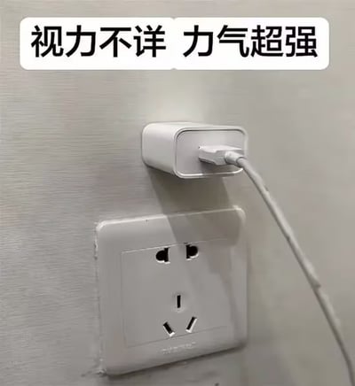 图片展示了一个白色墙壁插座，其上有一个白色插头被以明显倾斜的角度插入，插头并未准确对准插座的插孔，而是歪着强行插入，显得十分不协调。图片顶部有一行黑色文字“视力不详 力气超强”，幽默地调侃这种“看不清插孔却能用蛮力插插头”的生活趣事，充满了日常搞笑气息。