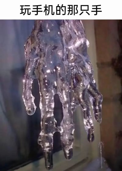 图片上方配有文字“玩手机的那只手”，下方是一个形似人手的冰雕或类似材质的雕塑。这个雕塑呈现出不规则的形状，表面光滑且有反光效果，整体呈现出一种晶莹剔透的质感，仿佛一只被冻结的手。图片通过将冰雕手与“玩手机”的文字结合，形成一种幽默的视觉联想，暗示现代人过度沉迷手机的状态。