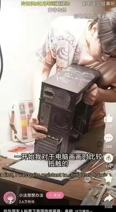 图中是一位戴眼镜的男生，正抱着电脑机箱，在机箱的外壳上手绘图案。结合图中的字幕“一开始我对于电脑画画时比较抵触的”以及底部的“给外国友人科普下我国传统画具：电脑”，玩了一个谐音梗——通常大家说的“电脑画画”是指用数位板在电脑软件里进行绘图创作，而这里的“电脑画画”被曲解成直接在电脑（机箱）的实体外壳上画画，形成了强烈的反差感，十分搞笑。画面上方的弹幕“你用的什么笔刷”也在配合这个梗，把手绘电脑机箱的行为当成数位板绘图来提问，进一步强化了这个整活的效果。