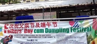这是一张户外拍摄的社区节庆活动宣传横幅照片，横幅以红、绿、白为主要色调，采用中英双语标注活动主题“庆祝父亲节及端午节（Fathers' Day cum Dumpling Festival）”。横幅上详细列出了活动信息：时间为2015年6月6日18:30-21:30，地点在Blk 706开放空间（新加坡组屋大牌706前广场），票价为5新元，售票地点在728西海岸健康俱乐部和Green RC中心。同时还标注了活动亮点，包括家庭包粽子比赛、家庭三人组比赛、父亲比赛，以及报名时间为5月11日至6月3日、报名费50新元，还有最高500新元现金券的幸运抽奖。背景是搭建的活动棚子，整体是为了宣传结合了父亲节与端午节的社区活动。