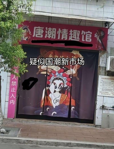 这是一家名为「唐潮情趣馆」的线下成人用品店铺，门头采用红色底搭配白色大字，两侧点缀古风戏曲人物图案；门帘使用国潮风格的原创戏曲卡通形象，人物戴着墨镜、手持折扇，造型新潮酷拽。店铺左侧竖牌标注「未成年人禁止入内」，图中还添加了文字标注「疑似国潮新市场」。
这里的「唐潮」谐音「唐朝」，用国风国潮的视觉风格包装成人用品店，形成传统与现代、国风与成人业态的反差感，让人觉得新奇。