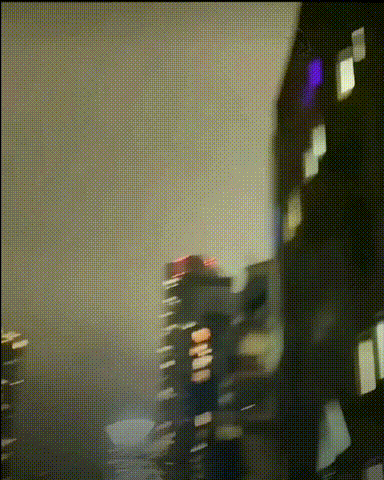 这是一段镜头晃动的GIF动态图，展现了夜晚的都市高楼景观。画面中几栋亮着灯光的摩天大楼矗立在昏暗的夜空下，镜头存在明显的晃动，整体画面略显模糊，营造出一种朦胧的夜晚城市氛围，图中没有出现人物或任何文字内容。