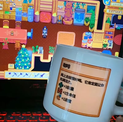 图片前景是一个白色咖啡杯，杯身贴有标签，写着“咖啡 闻上去就很好喝。它肯定能让你充满活力。+3 能量 +1 生命值 +1 速度”。背景是电脑屏幕显示的像素风格游戏画面，画面中有角色、家具、圣诞树等元素，右上角显示时间为上午9:30，还有数字83179221。整体呈现游戏玩家将现实咖啡想象成游戏内增益道具的趣味场景。