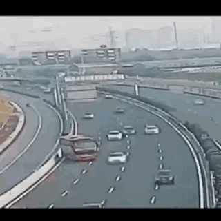 这是一段记录城市高速互通立交桥的动态图，画面中多条车道上的车辆在正常行驶，左侧匝道处一辆红色车辆在转弯过程中失控，车身偏移有冲出匝道的趋势，场景十分惊险，还原了真实的交通意外瞬间，具有交通安全警示意义。