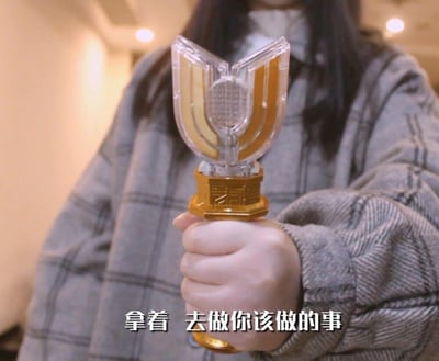 图中一位穿着格子大衣的人紧握迪迦奥特曼的变身道具神光棒，画面下方配有字幕“拿着 去做你该做的事”。这张图翻拍自《迪迦奥特曼》中传承变身器的经典热血场景，将原作中传承力量、肩负使命的氛围用生活化的方式呈现，常用于在社交场景中激励他人去完成应做的事，带有调侃又充满力量的感觉。