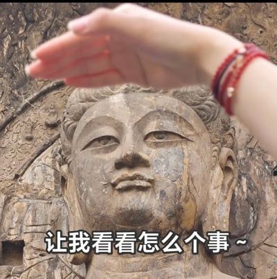 图片展示了一位游客对着大型石刻佛像举手作势的画面，下方配有文字“让我看看怎么个事~”，与佛像庄重的形象形成搞笑反差感。该动作模仿网络流行的互动表情包，常用以表达好奇、想要了解情况的心理，属于轻松幽默的互联网交流风格。图片通过手势和场景结合，可被用作日常吐槽或搞怪表达。