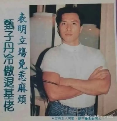 图片展示了甄子丹的一张早年写真照，他穿着白色短袖上衣和牛仔裤，双臂交叉站立，表情冷峻。照片左侧有竖排繁体中文字：“表明立塲免惹麻煩 甄子丹冷傲退基佬”。背景中可见几个大型白色花瓶，整体呈现出90年代的摄影风格。