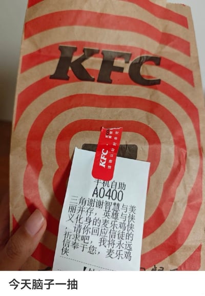 这张实拍静态图展示了一个肯德基的牛皮纸外卖袋，袋身印有红色同心圆环和黑色KFC品牌标识，袋口用印有KFC字样的红色封条贴住，封条下方贴着手机自助下单的订单小票，小票的备注栏写着大段玩梗文字：“三角谢谢智慧与美丽并存，英雄与侠义化身的麦乐鸡侠，请你回应信徒的祈求吧，我将永远信奉于您，麦乐鸡侠”，画面左下角露出了拍摄者的部分手指，图片最下方配有文字“今天脑子一抽”，体现了拍摄者突发奇想在肯德基订单上写麦当劳相关的麦乐鸡侠梗的趣味整活操作。