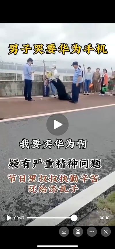 这是一段现场视频的截图，画面中一名黑衣男子跪在户外道路旁的人行道上，情绪崩溃地哭喊着要买华为手机，现场有两位执勤的警务人员在旁处理，还有多名路人驻足围观。图中配文标注该男子疑有严重精神问题，同时感慨节日里执勤的警务人员被添了麻烦。