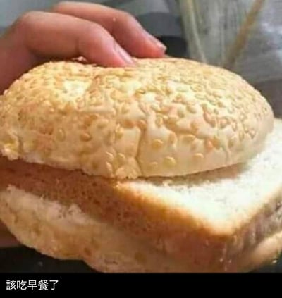 一只手正捧着一个表面撒满芝麻的金黄色面包，面包外皮看起来酥脆，内部松软。图片底部有一行文字“該吃早餐了”，整体给人一种温馨提醒的感觉，适合在早晨分享，鼓励大家按时吃早餐。