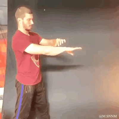 这是一段动态GIF，画面中一名身着酒红色T恤、深色带蓝条运动裤的男子，面对深色背景做出连贯的手部动作，手部动作同步配合出现的火焰特效，模拟出施展火焰魔法的场景，动作和特效结合自然，整体效果趣味十足，没有双关、谐音梗或暗示内容。