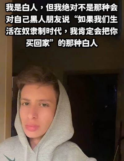 图片中是一位穿着灰色连帽衫的白人男性，他正在进行自拍。图片上方有一段文字：“我是白人，但我绝对不是那种会对自己黑人朋友说‘如果我们生活在奴隶制时代，我肯定会把你买回家’的那种白人”。这段文字通过幽默的方式揭示了某些白人试图表达友好却说出冒犯性言论的现象，反映了种族关系中的敏感性问题。