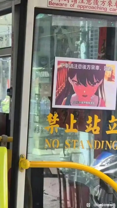 公交车窗上贴有官方的"禁止站立 NO STANDING"标识，同时被网友添加了一张动漫女孩海报。海报上的动漫女孩表情严肃，配文"下车请注意后方来车，因为那些司机虽然看起来很普通"，用幽默方式强调交通安全。