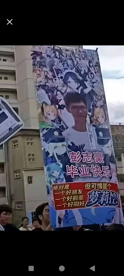 这是一张大学毕业典礼现场的合影照片，有人在现场高举着自制的二次元风格海报。海报上汇集了多位二次元美少女角色，并且用大字写着“彭志豪 毕业快乐”。下方的段子文案“毕业是一个好朋友 一个好前妻 一个好同好 但可惜是梦莉娅”巧妙调侃毕业礼物总是动漫老婆（虚拟角色）的现象，也暗含对现实与二次元的对比，讽刺了毕业时只能收到“纸片人老婆”的无奈。整体氛围轻松诙谐，带有二次元和宅文化圈的自嘲气质。

**有显著的二次元梗、“纸片人老婆”双关自嘲。**
