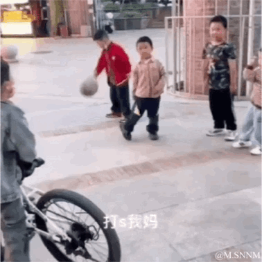 这是一段户外场景的动态图，画面中几个孩童在空地上玩耍，一名穿红色上衣的小孩正专注地拍着篮球，画面下方配有文字“打s我妈”，利用孩童发音的谐音梗制造反差笑点，实际孩童的话语应该和拍球相关，却被谐音成具有冲击力的“打死我妈”，形成荒诞搞笑的效果。