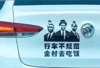 这是一张原始拍摄的静态图文混排图，展示了一辆白色别克汽车的车尾区域。车尾张贴了一张创意警示车贴，车贴上方是三个穿着黑色正装、戴着礼帽与墨镜的黑人形象，该形象源自网络爆火的“黑人抬棺”热梗；车贴下方配有黑色简体中文文字“行车不规范 全村去吃饭”，这句话改编自电影《流浪地球》中的经典交通安全警示语“行车不规范，亲人两行泪”，用夸张戏谑的方式调侃不规范驾驶可能带来的严重后果，以此提醒驾驶员遵守交通规则，兼具趣味性与警示性。