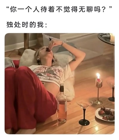 这是一张图文结合的生活类梗图，上方文字以旁人的疑问“你一个人待着不觉得无聊吗？”引出，随后用“独处时的我：”衔接下方画面。画面中一位女性惬意地躺在室内地板的垫子上，姿态慵懒放松，一只手将食物送入口中，身旁摆放着酒瓶、高脚杯、点燃的蜡烛和甜点，整体氛围舒适自在，用实际状态回应了“独处是否无聊”的疑问，展现出独处时的享受与惬意，打破了“独处=无聊”的刻板印象。
