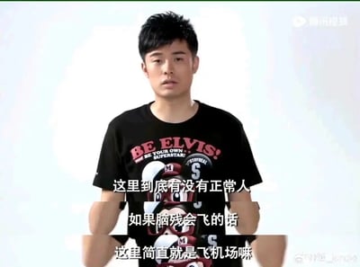 这是都市情景喜剧《爱情公寓》的经典截图，画面中是由演员陈赫饰演的角色曾小贤，他身着印有“BE ELVIS! BE YOUR OWN SUPERSTAR!”字样的黑色卡通图案T恤，脸上露出无奈又无语的神情，正对着镜头方向发出吐槽。图中的字幕是他的经典台词：“这里到底有没有正常人，如果脑残会飞的话，这里简直就是飞机场嘛”，用夸张且诙谐的比喻，表达了对身边人和事的不满与吐槽，充满搞笑氛围，是剧中广为人知的名场面，常被网友用作表达对周遭离谱事物的吐槽素材。